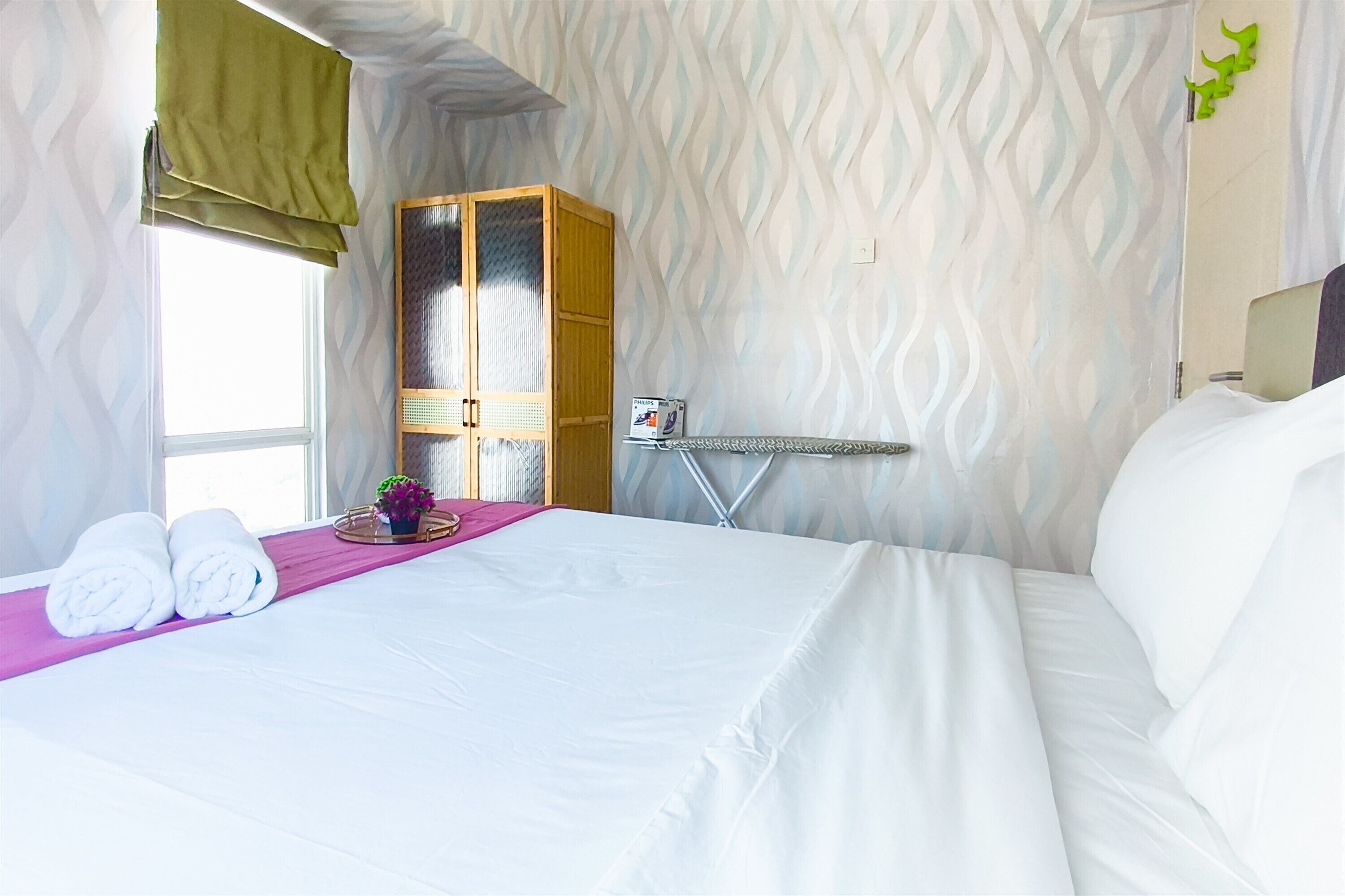A hotel room with a bed, a wardrobe, a window, and a wall-mounted ironing board.