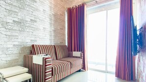 Ein Zimmer mit einem gestreiften Sofa, einer Bank, einer Ziegelwand und einem großen Fenster mit Vorhängen.
