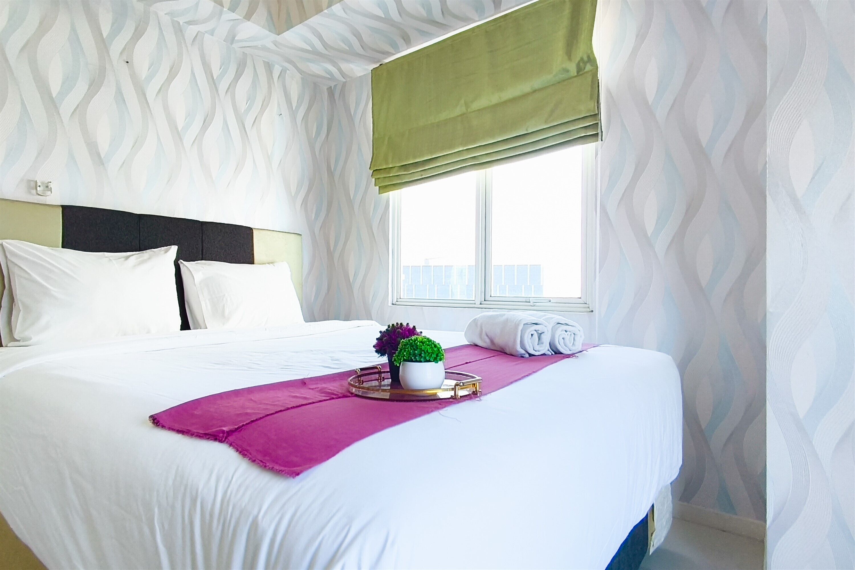 A neatly made bed with white linens, a purple throw, and a small potted plant on a tray.