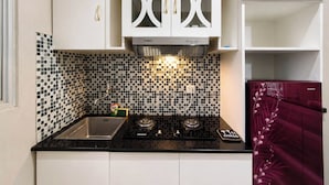 A compact kitchen with white cabinets, black and white tiled backsplash, a gas stove, and a red appliance. - Serene 2Br Apartment Newton Residence Bandung (Bandung)