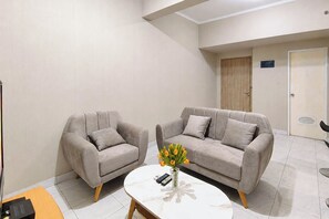 Ein modernes Zimmer mit zwei grauen Sofas, einem kleinen weißen Tisch mit Blumenvase und einer Tür im Hintergrund.