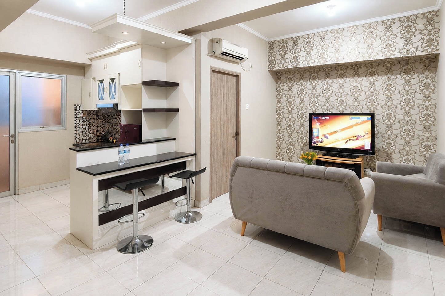 A modern living room with a sofa, a TV, and a kitchen area with a bar.
