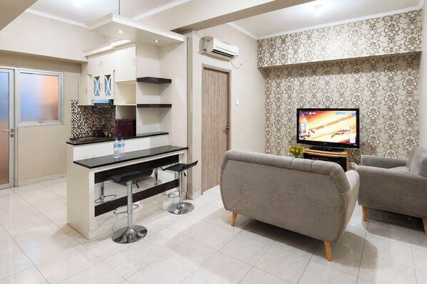 Una sala moderna con sofá, televisión y una zona de cocina con barra.