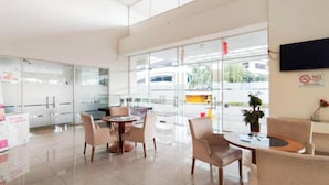 A hotel lobby with a reception desk, seating area, and large windows offering a view of the street. - Serene 2Br Apartment Newton Residence Bandung (Bandung)