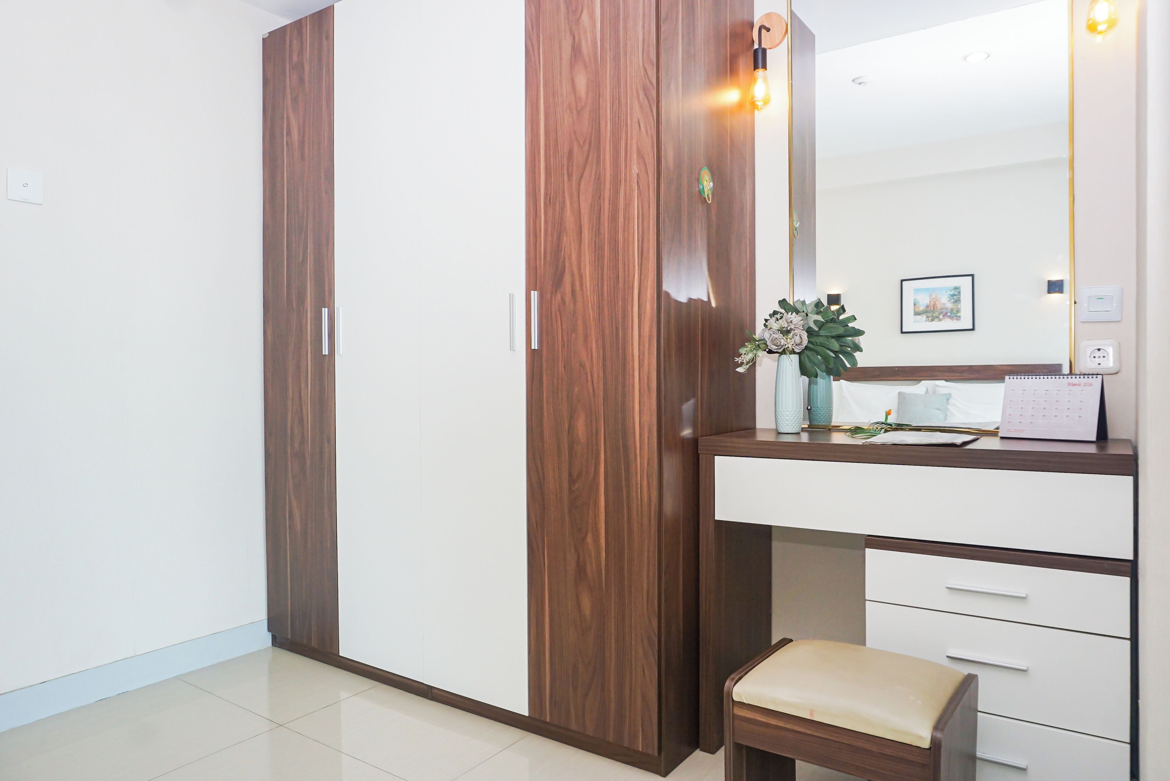 A room with a wooden wardrobe, a vanity with a mirror, and a small stool.