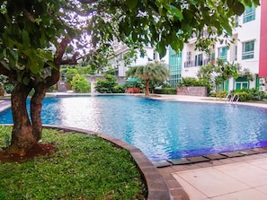 A swimming pool surrounded by greenery and a building with multiple windows. - Good Designed 2Br Apartment Woodland Park Residence (Jakarta)