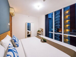A hotel room with a large bed, a bedside table, a mirror, and a window with a city view. - Good Designed 2Br Apartment Woodland Park Residence (Jakarta)