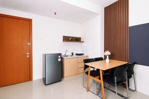 A compact kitchen with a refrigerator, a sink, and a wooden dining table with chairs. - Stunning 2Br Apartment Woodland Park Residence (Jakarta)