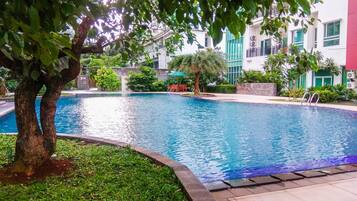 A swimming pool surrounded by greenery and a building with multiple windows.