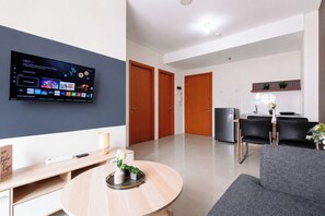A modern living room with a flat-screen TV, a round wooden table, and a grey sofa. - Stunning 2Br Apartment Woodland Park Residence (Jakarta)