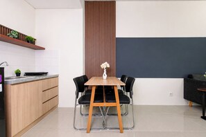 A modern kitchen with a dining area, featuring a wooden table and chairs, a vase with flowers, and a vertical wooden panel. - Stunning 2Br Apartment Woodland Park Residence (Jakarta)