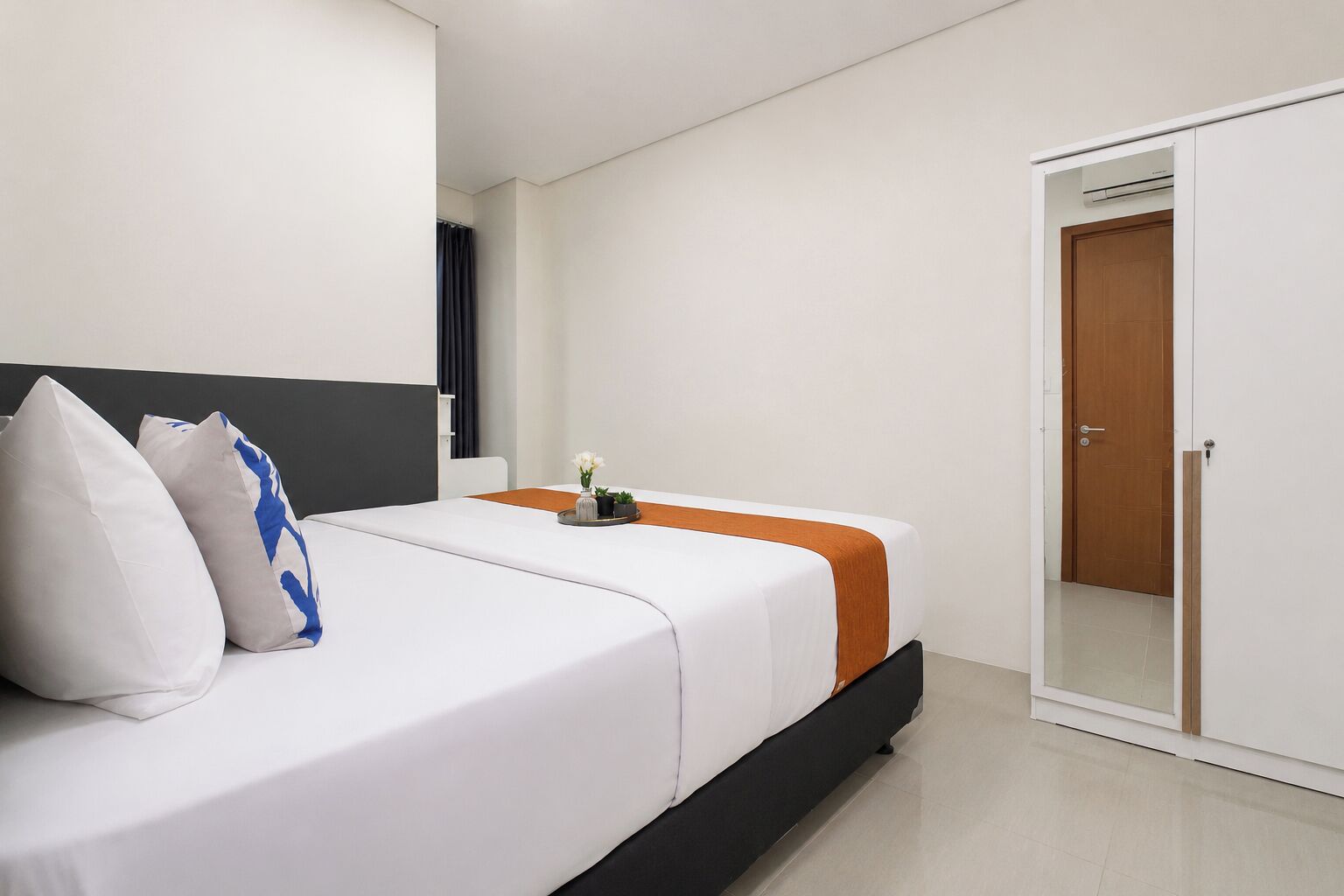 Una habitación de hotel moderna con una cama, una mesita de noche con un florero y un armario.