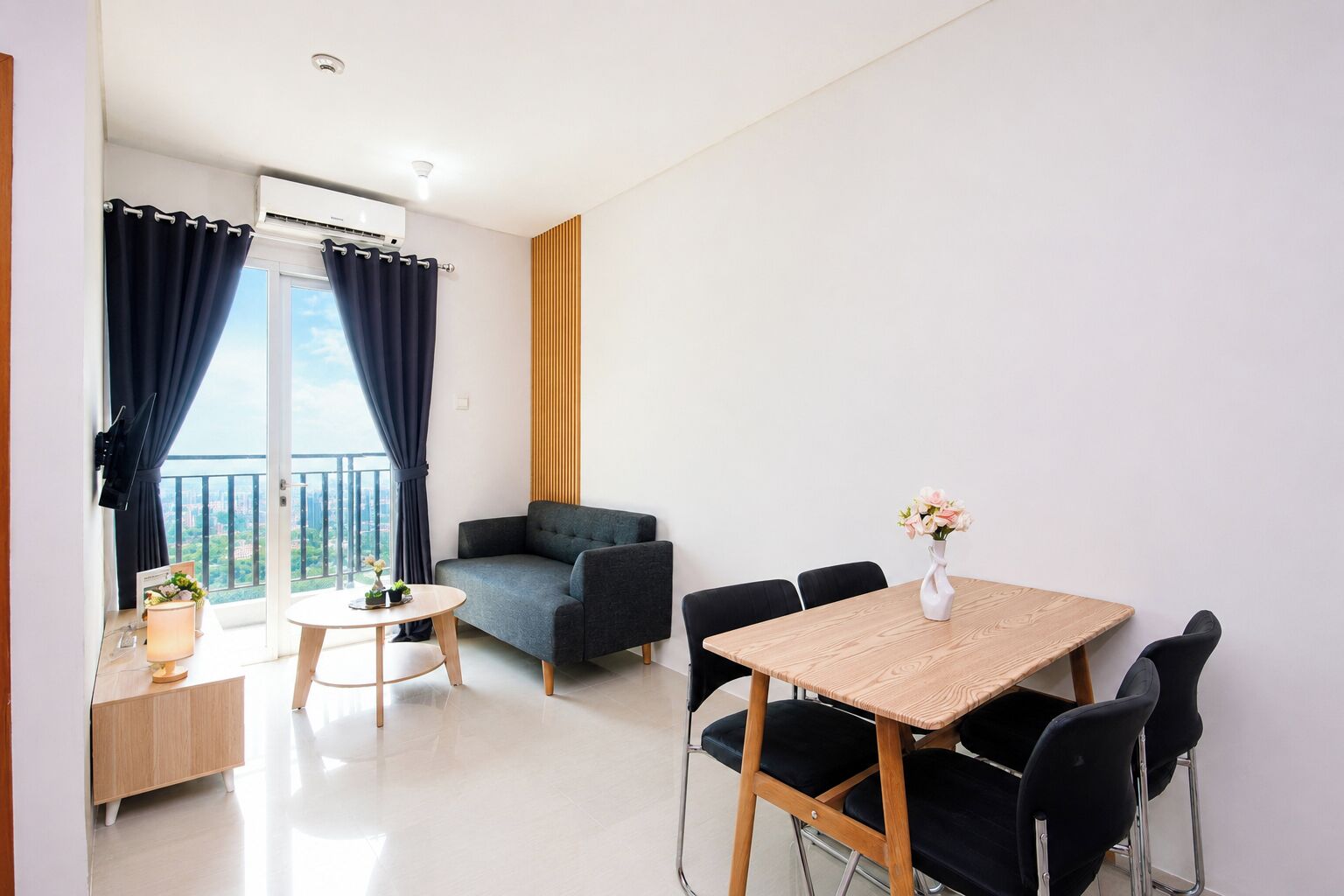 Een moderne woonkamer met een bank, een ronde tafel en een eettafel met stoelen. Er is een balkon met gordijnen en uitzicht op de stad.