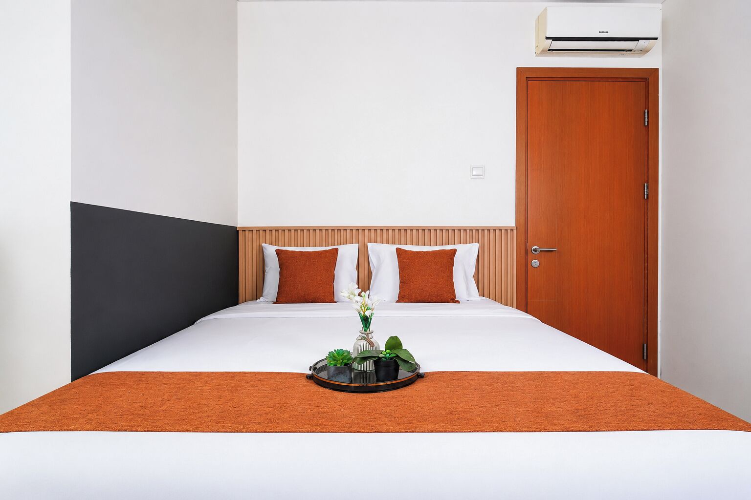 A hotel room with a bed, a wooden door, and an air conditioning unit on the wall.
