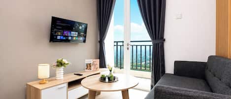 Una sala de estar moderna con un sofá, una mesita redonda, un televisor montado en la pared y un balcón con cortinas.