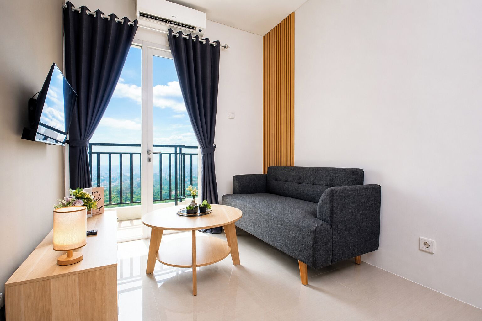 A modern living room with a grey sofa, a round wooden table, and a TV mounted on the wall.