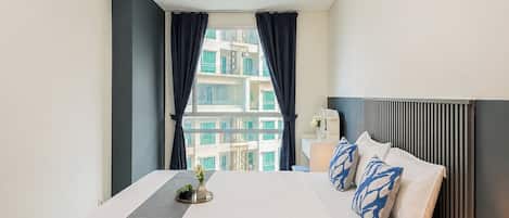 Habitación de hotel con una cama, una mesita de noche, una lámpara y vistas a un edificio por la ventana.