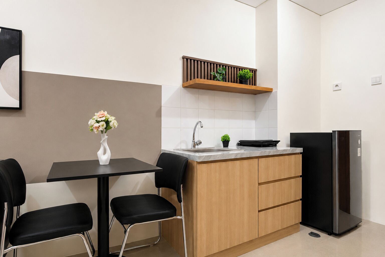 Eine moderne Küche mit einem schwarzen Kühlschrank, einem Holzschrank, einer schwarzen Arbeitsplatte, einem Waschbecken und einer Tischvase mit Blumen.
