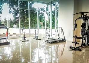 A gym with various exercise equipment, large windows, and a clean, reflective floor. - Chic Cozy 1Br Apartment Woodland Park Residence (Jakarta)