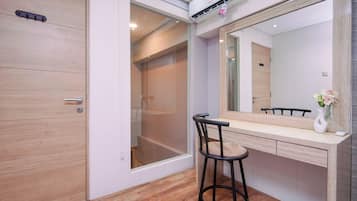 Une salle de bain avec une porte en bois, un espace douche, un meuble-lavabo avec un miroir et un tabouret.