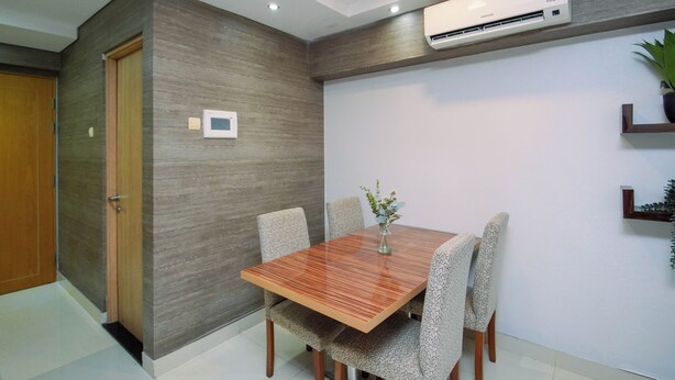 Un comedor moderno con una mesa de madera y sillas estampadas, un equipo de aire acondicionado en la pared y una planta en maceta sobre una estantería.