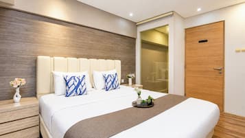 A modern hotel room with a large bed, a wooden headboard, a nightstand with a vase of flowers, and a wooden door.