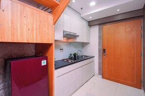 A compact kitchen with a built-in refrigerator, a sink, and a wooden door. - Restful And Roomy Loft 2Br At Apartment Maqna Residence (Jakarta)