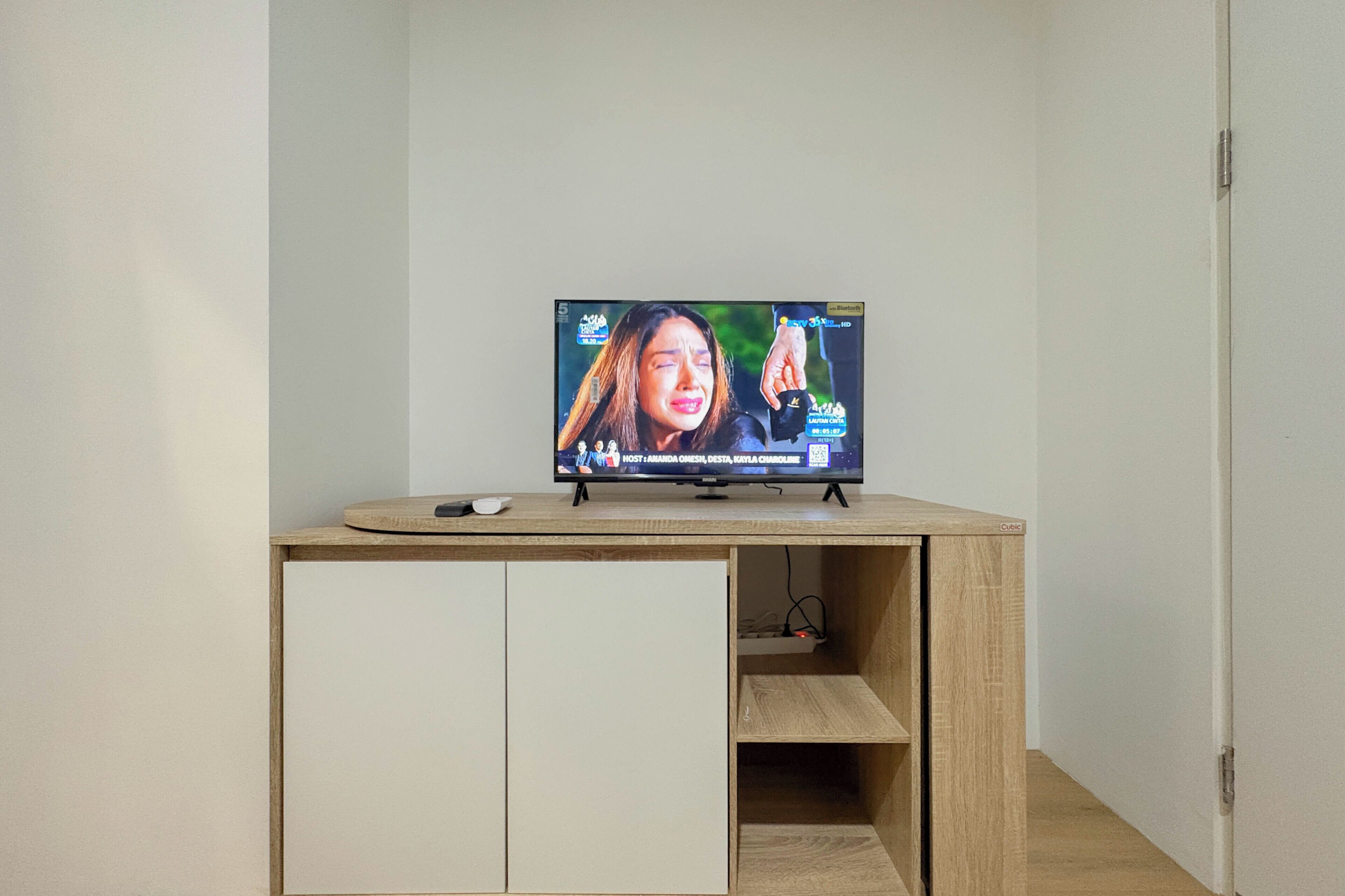 A television on a wooden desk with a remote control and a smartphone.