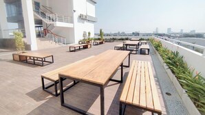A rooftop terrace with outdoor seating, a staircase, and a view of the city skyline. - Cozy Japandi Style 1Br At Apartment Kyo Society (Surabaya)