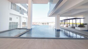 A modern indoor swimming pool with a view of the cityscape, surrounded by white walls and a tiled floor. - Cozy Japandi Style 1Br At Apartment Kyo Society (Surabaya)