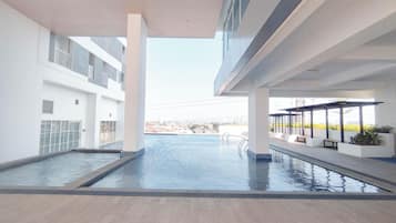A modern indoor swimming pool with a view of the cityscape, surrounded by white walls and a tiled floor.
