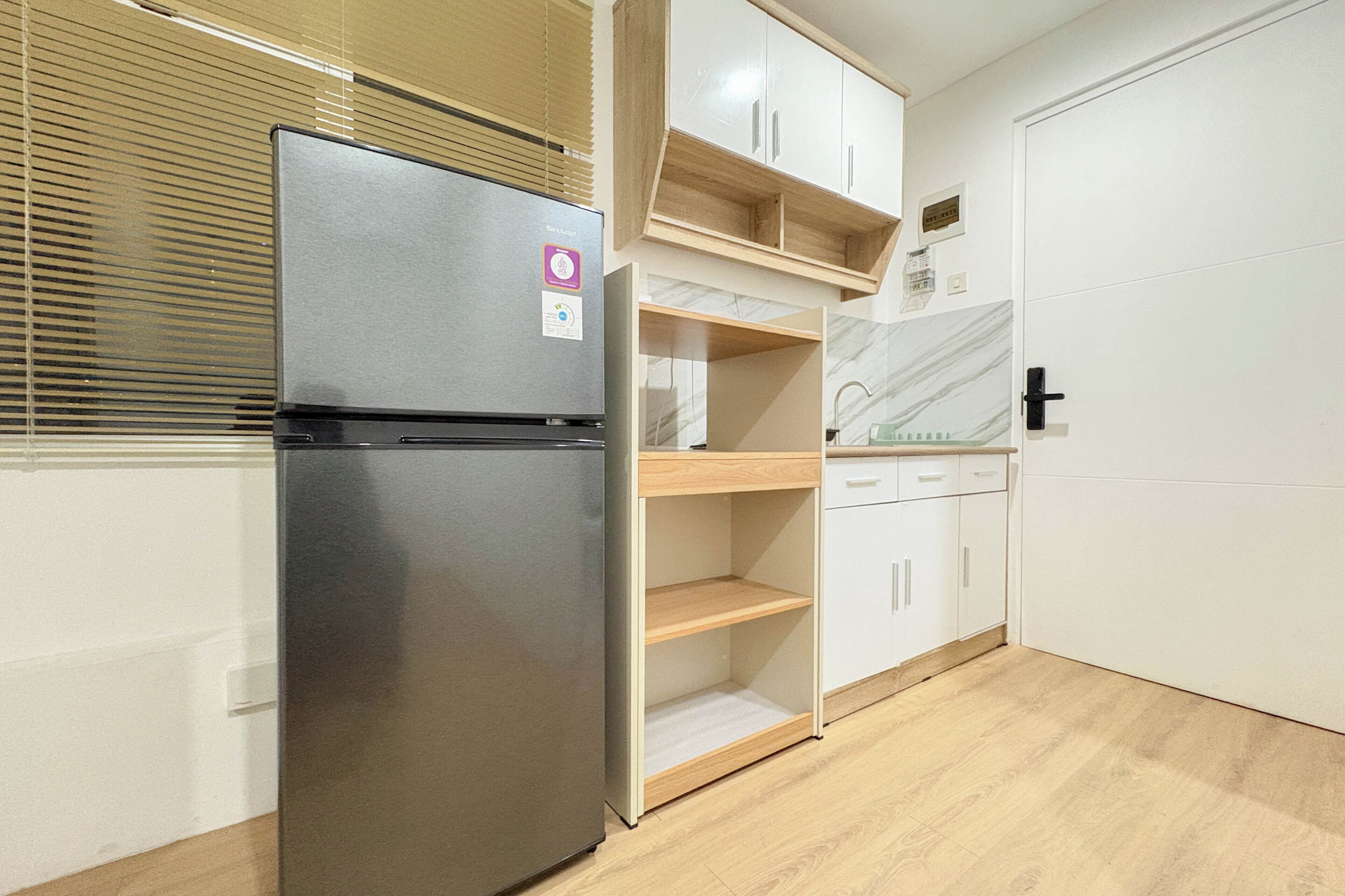 Une cuisine compacte dotée d’un réfrigérateur intégré, d’étagères en bois et d’une porte blanche.