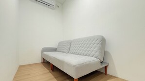 A minimalist room with a grey sofa, a small side table, and a wooden floor. - Cozy Japandi Style 1Br At Apartment Kyo Society (Surabaya)