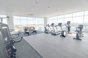 Et fitnesscenter med træningsudstyr, store vinduer og udsigt over byen.