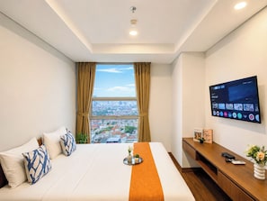 Quarto de hotel com cama, escrivaninha, televisão e janela com vista para a cidade.