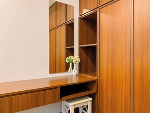 A wooden vanity with a mirror, a vase with flowers, and a small stool. - Graceful And Classic 2Br At Apartment The Kencana Residence (Jakarta)