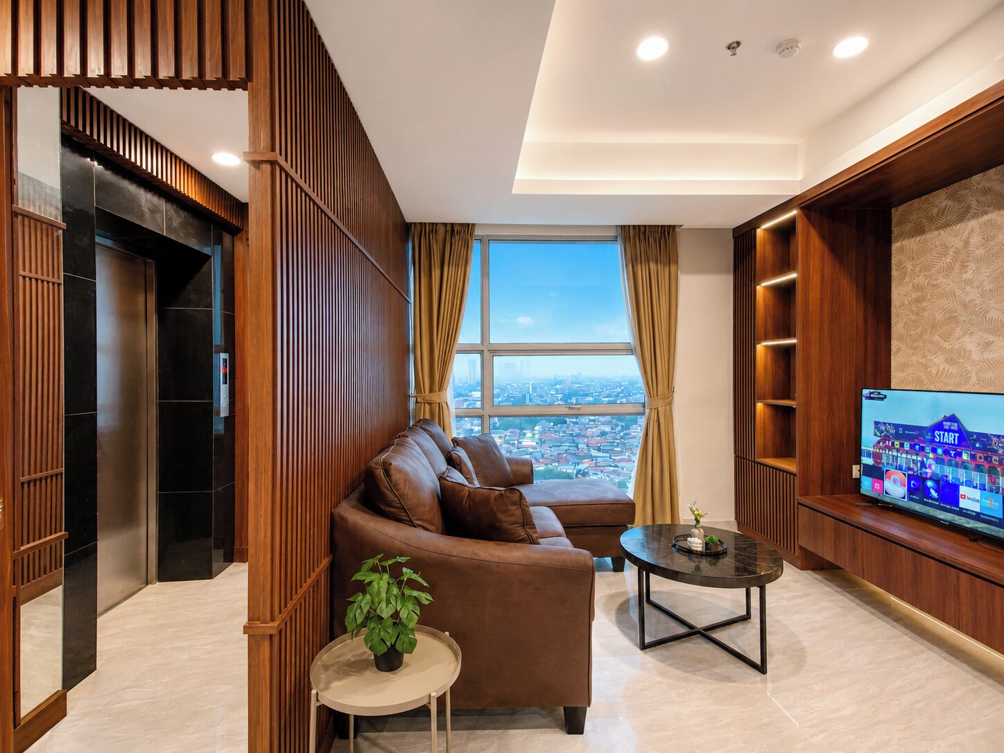 A modern living room with a leather sofa, a small round table, a potted plant, and a television on the wall.