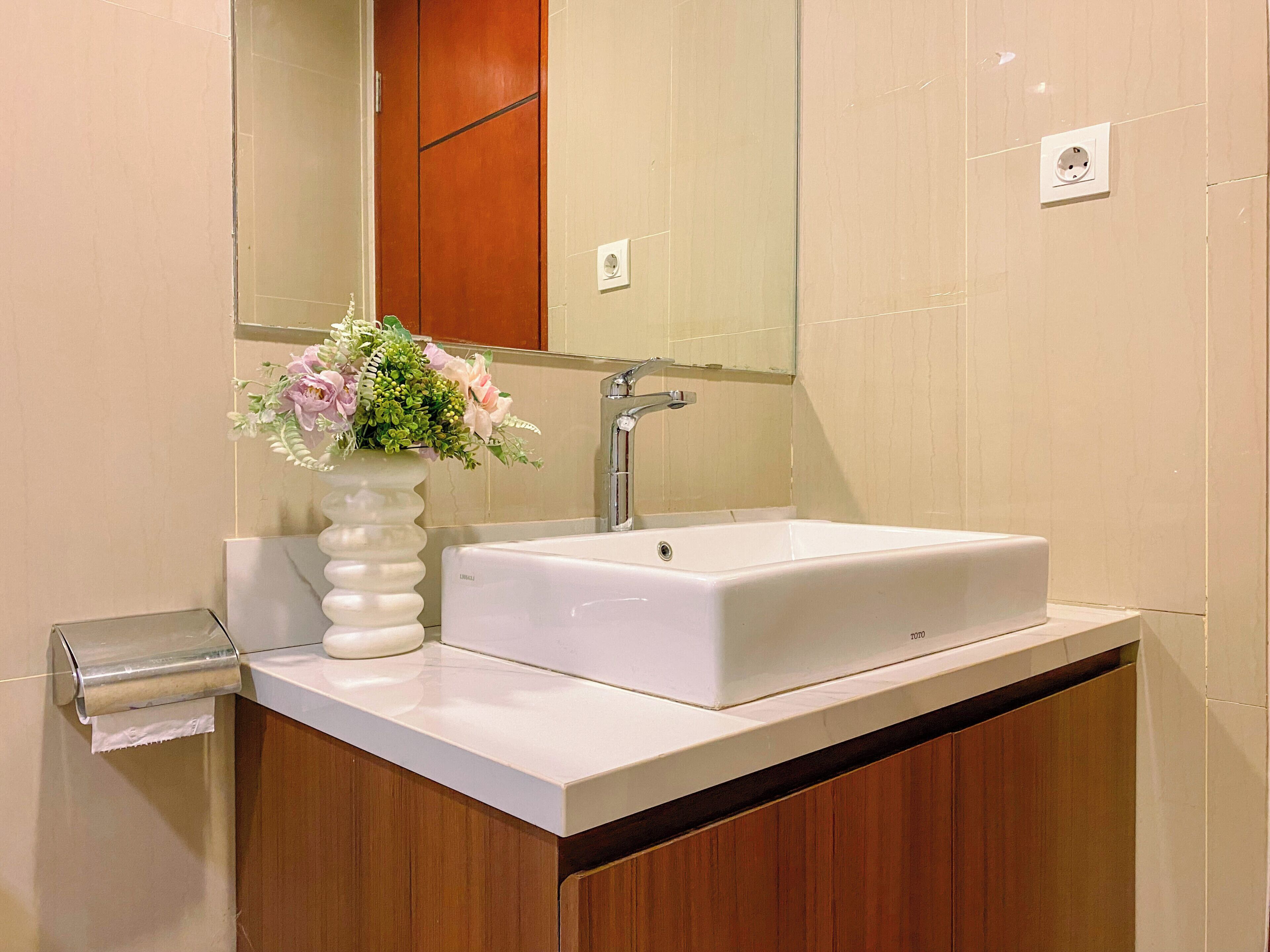 A bathroom with a white sink, a mirror, a wooden cabinet, and a vase with flowers.