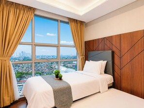 A hotel room with a large window, a bed, a bedside table with a plant, and a wooden accent wall. - Graceful And Classic 2Br At Apartment The Kencana Residence (Jakarta)