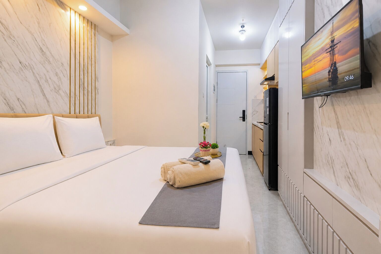 A hotel room with a bed, a TV, a small kitchenette, and a door leading to another room.