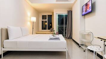 A hotel room with a bed, a TV, a bedside table, and a small balcony with a view.