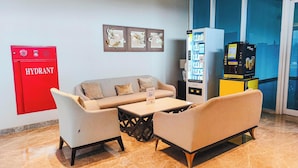 A hotel lobby with a sofa, chairs, a coffee machine, a vending machine, and a red hydrant. - Well Appointed Studio At Apartment Westown View Surabaya (Surabaya)