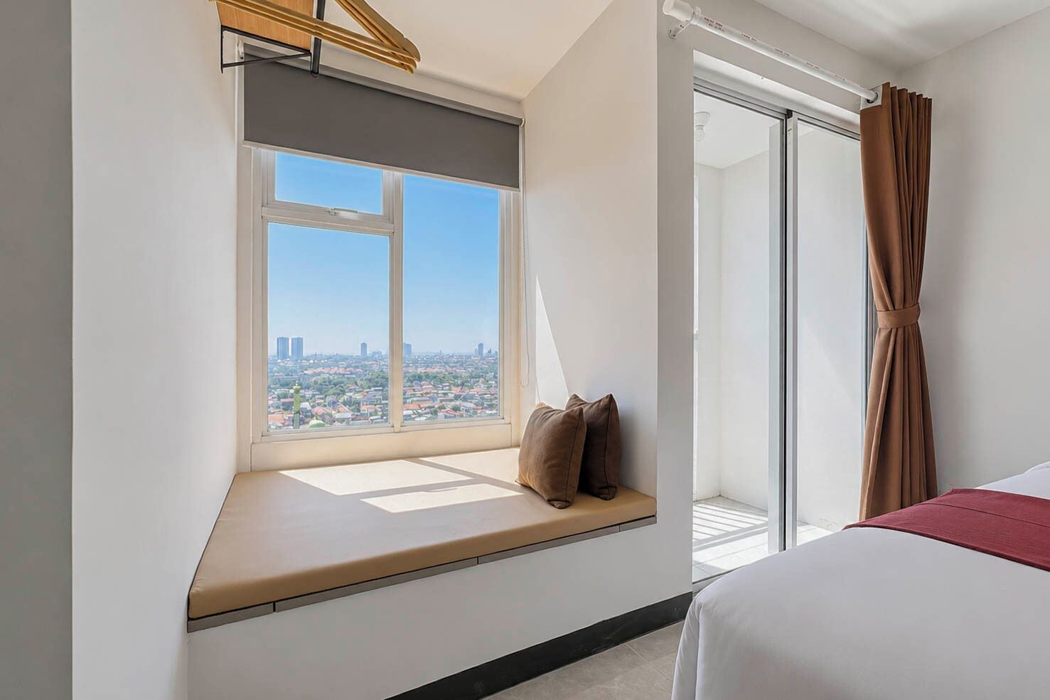 A hotel room with a large window, a bed, and a view of a cityscape.