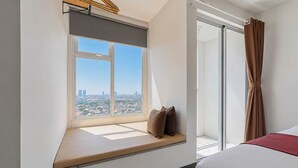 Ett hotellrum med ett stort fönster, en säng och utsikt över stadsbilden.