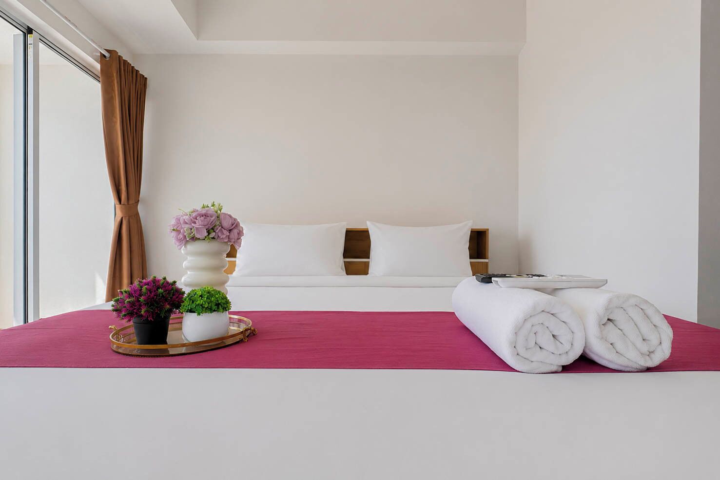 Habitación de hotel con una cama, almohadas, una mesita de noche con un jarrón de flores y toallas dobladas.