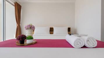 Habitación de hotel con una cama, almohadas, una mesita de noche con un jarrón de flores y toallas dobladas.