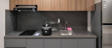A modern kitchen with a built-in induction cooktop, a coffee maker, a sink with a faucet, and a stainless steel refrigerator.