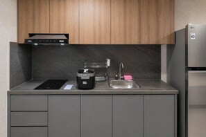 Eine moderne Küche mit integriertem Induktionskochfeld, einer Kaffeemaschine, einem Spülbecken inklusive Armatur und einem Edelstahlkühlschrank.