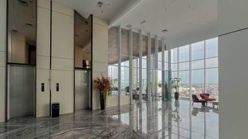 A spacious lobby with a marble floor, elevators, and large windows offering a city view.
