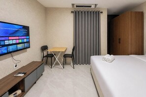 Een hotelkamer met een bed, een bureau met een computer, een televisie en een raam met gordijnen.